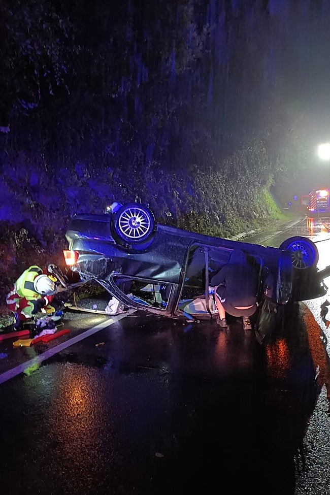 Los bomberos trabajan en el coche volcado en Saro.