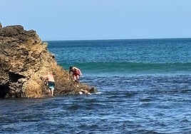 El hombre se agarra a la roca, mientras en el agua el ertzaintza sujeta a la mujer exhausta y el hombre del bañador rojo se acerca para ayudarlos.