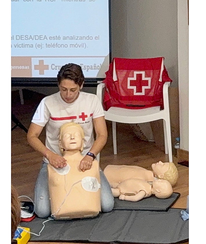 Imagen secundaria 2 - Asistentes al taller, realización de la maniobra de Heimlich con una voluntaria, y Tamara Alonso enseñando a colocar los parches del desfibrilador