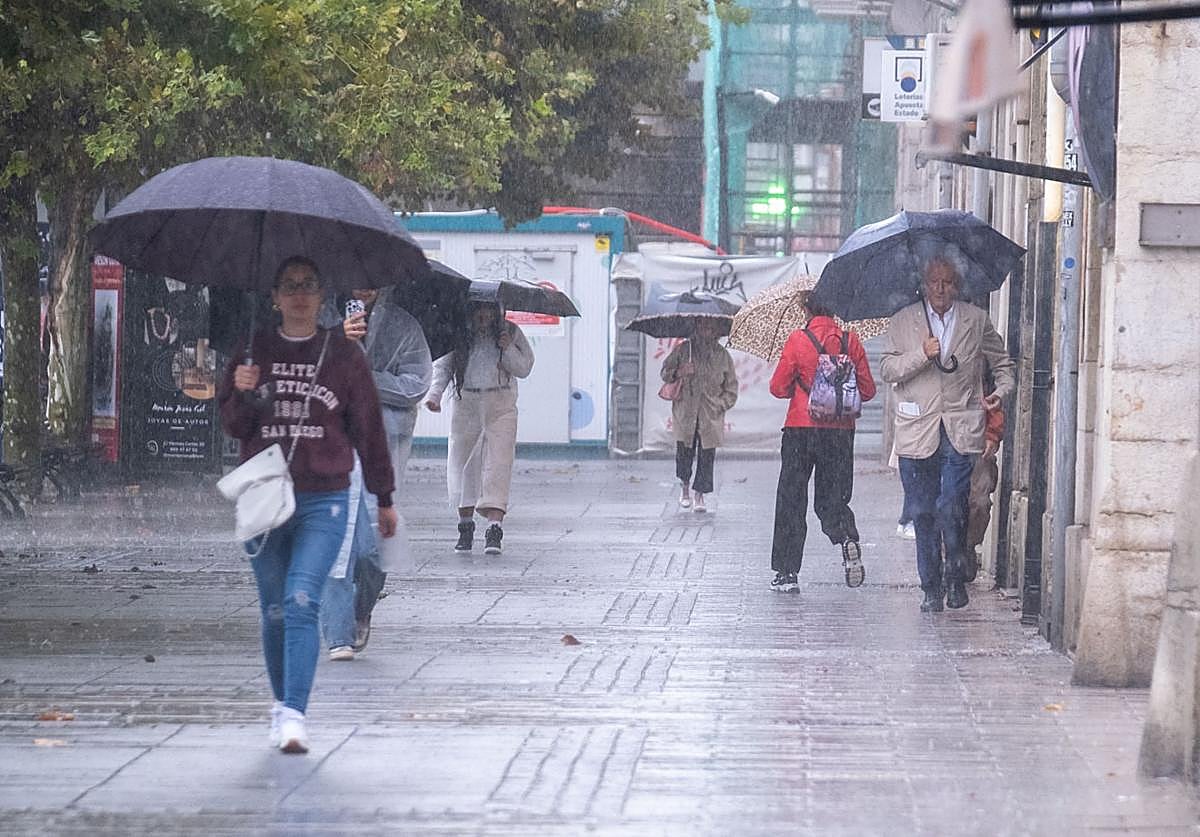 Viandantes se refugian con su paraguas de la intensa lluvia caída este lunes en Santander.