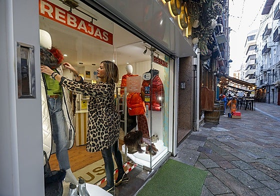 Una mujer coloca la prenda de un escaparate en rebajas de un comercio de Santander.
