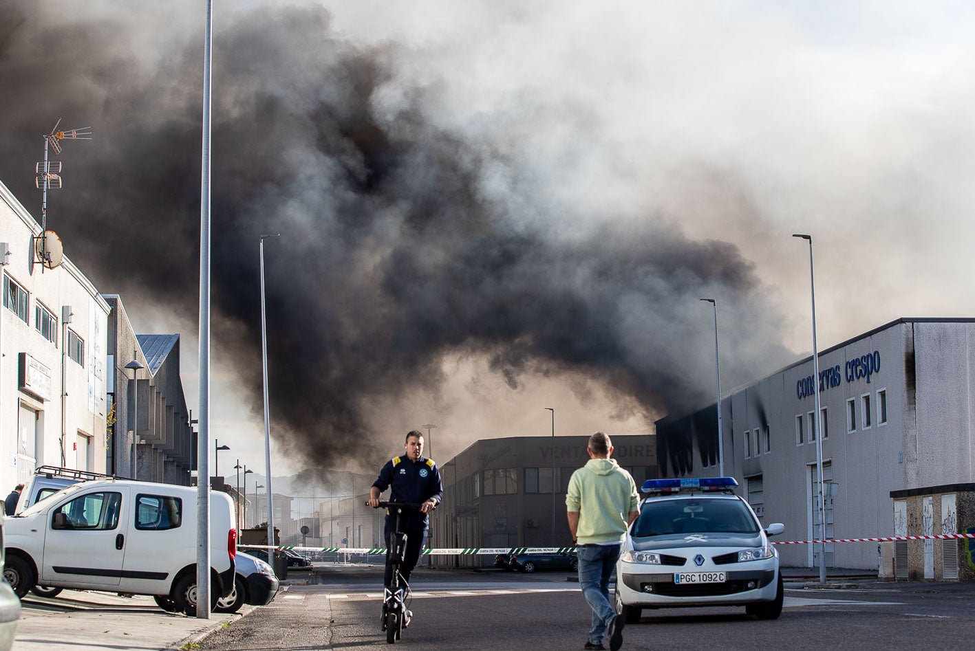 Un hombre en patinete se aleja del humo, mientras otro se acerca al cordón policial establecido