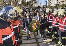 La alcaldesa pasa con una corona de laurel para colocarla en el monumento a los fallecidos, flanqueada por los cuerpos policiales y los bomberos.