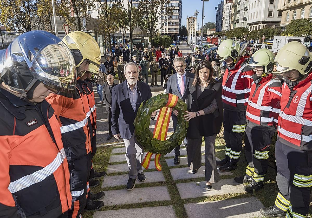 La alcaldesa pasa con una corona de laurel para colocarla en el monumento a los fallecidos, flanqueada por los cuerpos policiales y los bomberos.