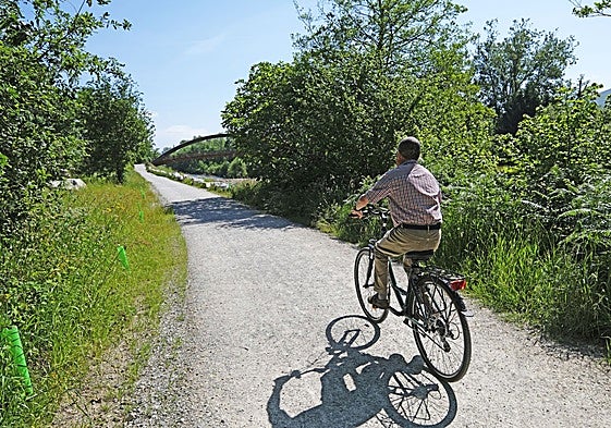 Un hombre en bicicleta atraviesa la senda en torno al río Saja en Cabezón de la Sal.