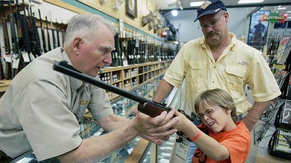 Un niño, acompañado por su padre, prueba un rifle en una tienda de armas. 