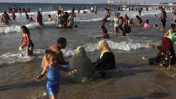 Mujeres vestidas, hombres y niños se bañan en una playa de Alejandría (Egipto).