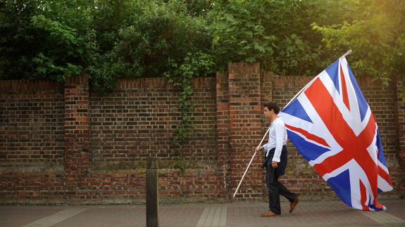 Un joven camina por una calle de Londres con una bandera británica.