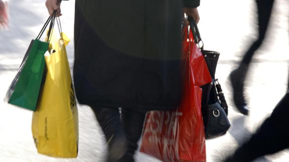 Una mujer camina cargada con bolsas de compra.