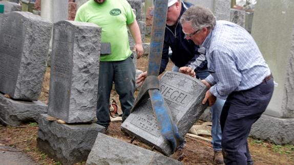 Varios hombres ayudan a reparar una lápida. 