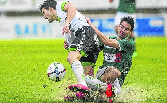 Álvaro Peña sufre una furete entrada en el campo del Coruxo, donde la lluvia embarró el terreno de juego. 
