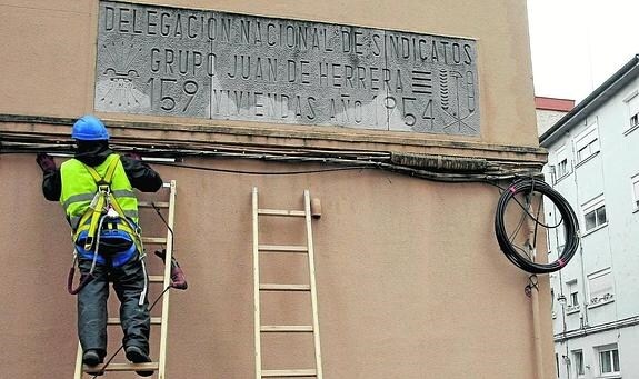 Un operario de telefonía trabaja junto a un edificio de La Inmobiiliaria que aún conserva una placa de simbología franquista.