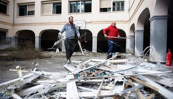 Dos obreros recogen piezas metálicas en el patio del colegio, como paso previo al derribo del edificio, que se desarrollará en las próximas semanas. 