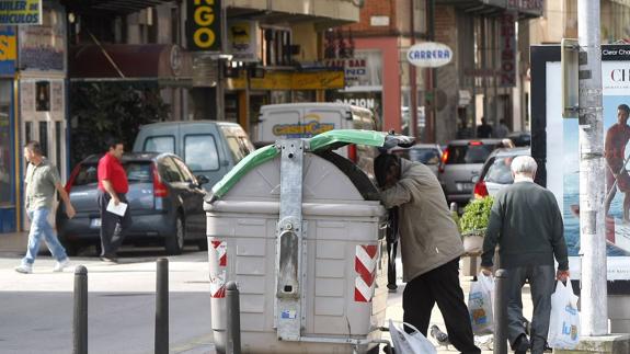 Indigente buscando en contenedor de basura.