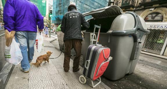 Una persona busca entre la basura de uno de los contenedores de la calle Cervantes, en Santander.