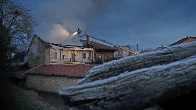 En primer término, un tejado cubierto de escarcha mientras los bomberos sofocaban el fuego en una vivienda de Udías.