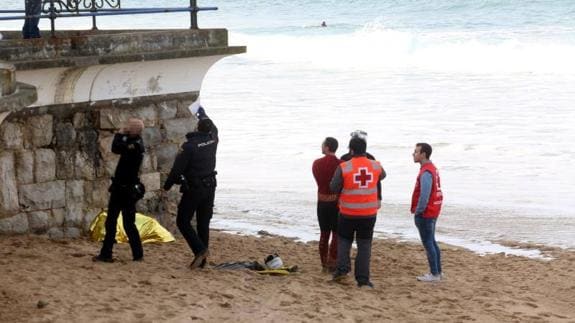 Agentes y efectivos de Cruz Roja, junto al cuerpo tapado con una manta en la playa de El Camello.