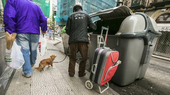 Una persona busca entre la basura de uno de los contenedores de la calle Cervantes, en Santander.