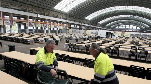 Dos operarios preparan las mesas y las sillas en el Ferial