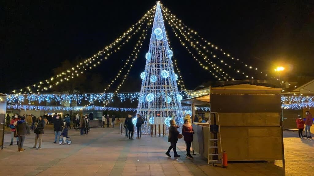 El árbol de Navidad preside el centro de la Plaza España de La Flecha rodeado de los puestos y atracciones que conforman el Mercado de Navidad de Arroyo de la Encomienda. 