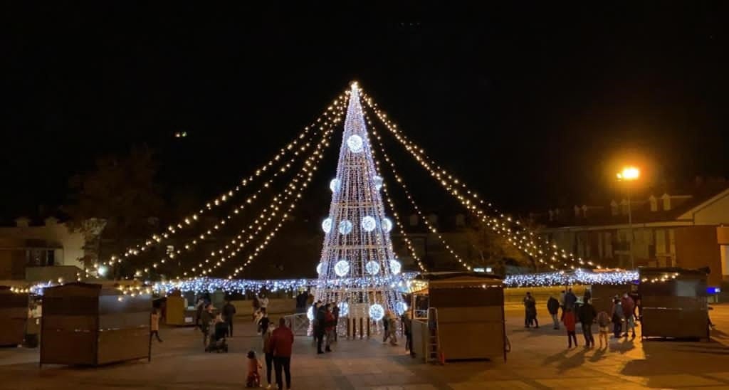 El árbol de Navidad preside el centro de la Plaza España de La Flecha rodeado de los puestos y atracciones que conforman el Mercado de Navidad de Arroyo de la Encomienda. 