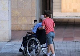 Un niño traslada a un anciano en silla de ruedas.