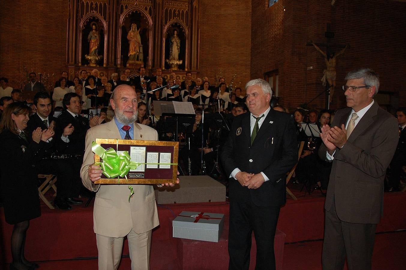 Claudio Prieto muestra el obsequio que le regaló el alcalde, Juan Jesús Blanco, en presencia del presidente de la Agrupación Musical de Guardo, Gerardo Compadre.