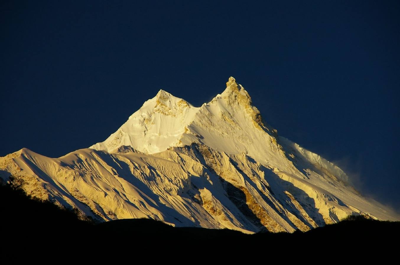 08 Manaslu. Su nombre, que significa 'Montaña de los Espíritus'. Con 8.156 m. sobre el nivel del mar, es la montaña más alta del Distrito Lamjung y está situada a unos 70 kilómetros al este del Annapurna. Sus largas aristas y valles glaciares ofrecen aproximaciones accesibles desde todas las direcciones y culmina en un pico que corona abruptamente el paisaje circundante, creando una silueta muy prominente vista desde la lejanía.