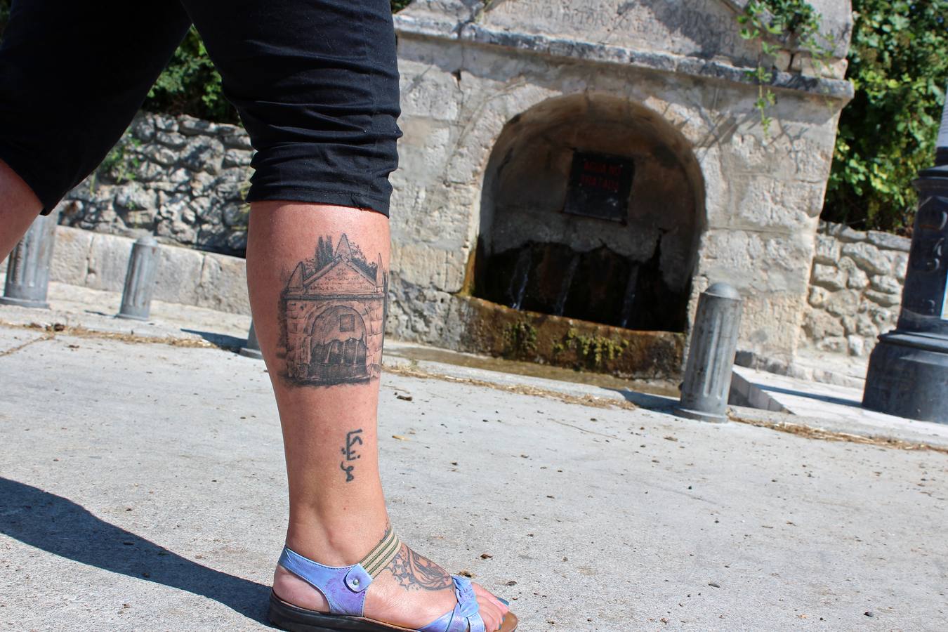 Elisa Cerrillo muestra su tatuaje del caño de San Pelayo con la fuente al fondo.