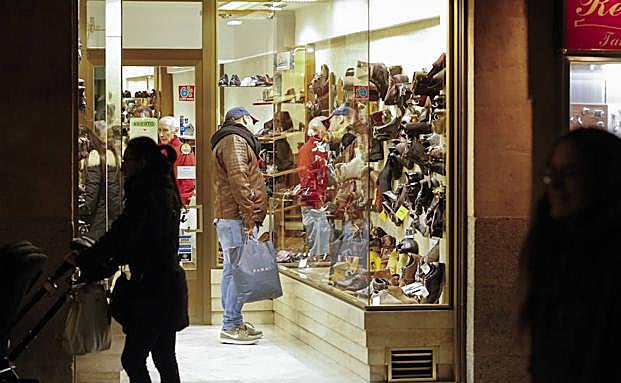 Los consumidores contemplan los artículos expuestos en el escaparate de un establecimiento comercial de la ciudad. 