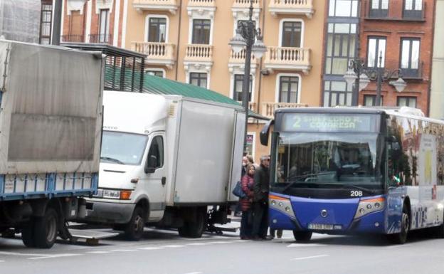 Varios pasajeros suben al autobús entre las furgonetas aparcadas en plaza de España. 