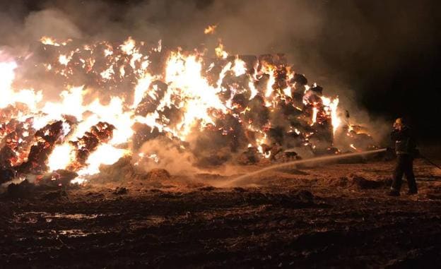 Un bombero echa agua a las pacas ardiendo. 