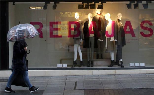 Una persona, paraguas en ristre, pasa ante un escaparate de rebajas en Valladolid.