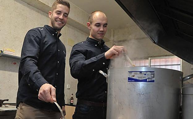 Héctor González y Adrián Fernández manipulan los pucheros del cocido solidario. 