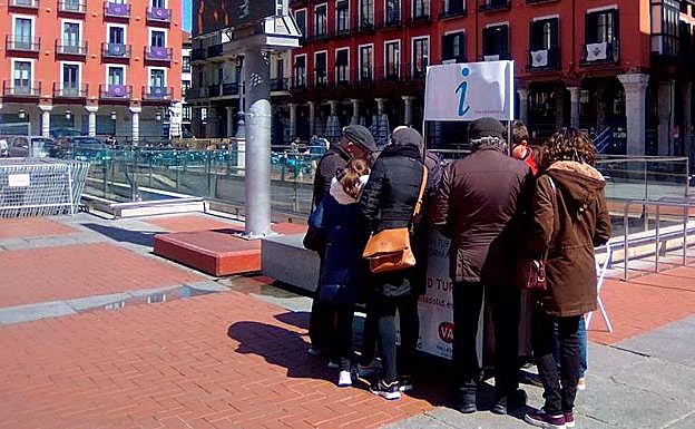 Varios turistas prestan atención a las indicaciones en un puesto de información en la Plaza Mayor.
