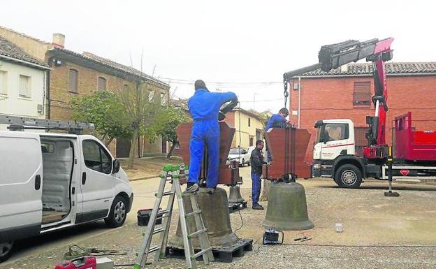 Dos operarios trabajan en la fijación del eje de las campanas, a los pies de la iglesia de Villafrades.