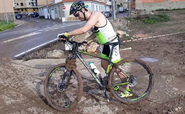 Un participantes conduce su bicicleta repleta de barro por la lluvia. 