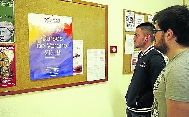 Dos alumnos buscan información sobre la oferta universitaria estival en un cartel colocado en los pasillos de su facultad. 