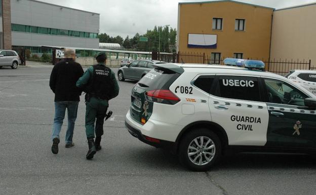Un guardia civil conduce a uno de los detenidos hasta el coche patrulla. 