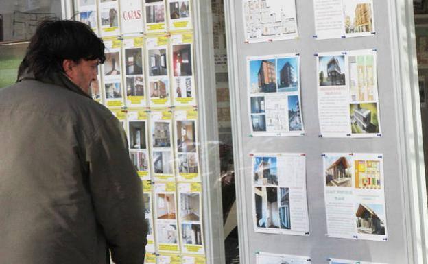Un hombre observa anuncios de venta de pisos en el escaparate de una inmobiliaria. 