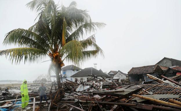 Dos hombres caminan entre escombros y propiedades dañadas en una playa de Sumur después del tsunami.