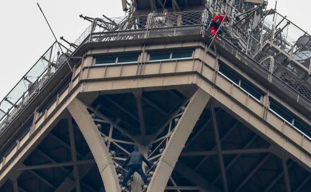 El escalador se para bajo uno de los ángulos de las estructuras más altas de la Torre Eiffel, mientras un bombero trata de descolgarse.