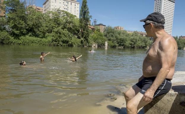 Un hombre observa a un grupo de jóvenes bañándose en la playa de Las Moreras de Valladolid.
