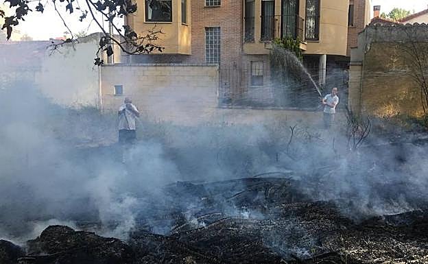 Dos vecinos utilzan sus mangueras para apagar ayer e fuego.