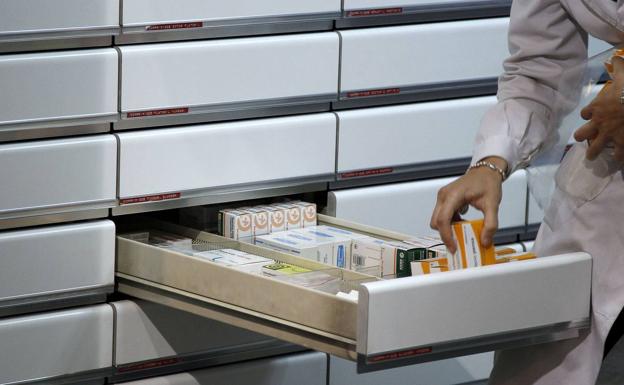 Una farmacéutica coloca varias cajas de medicamentos en una cajón.