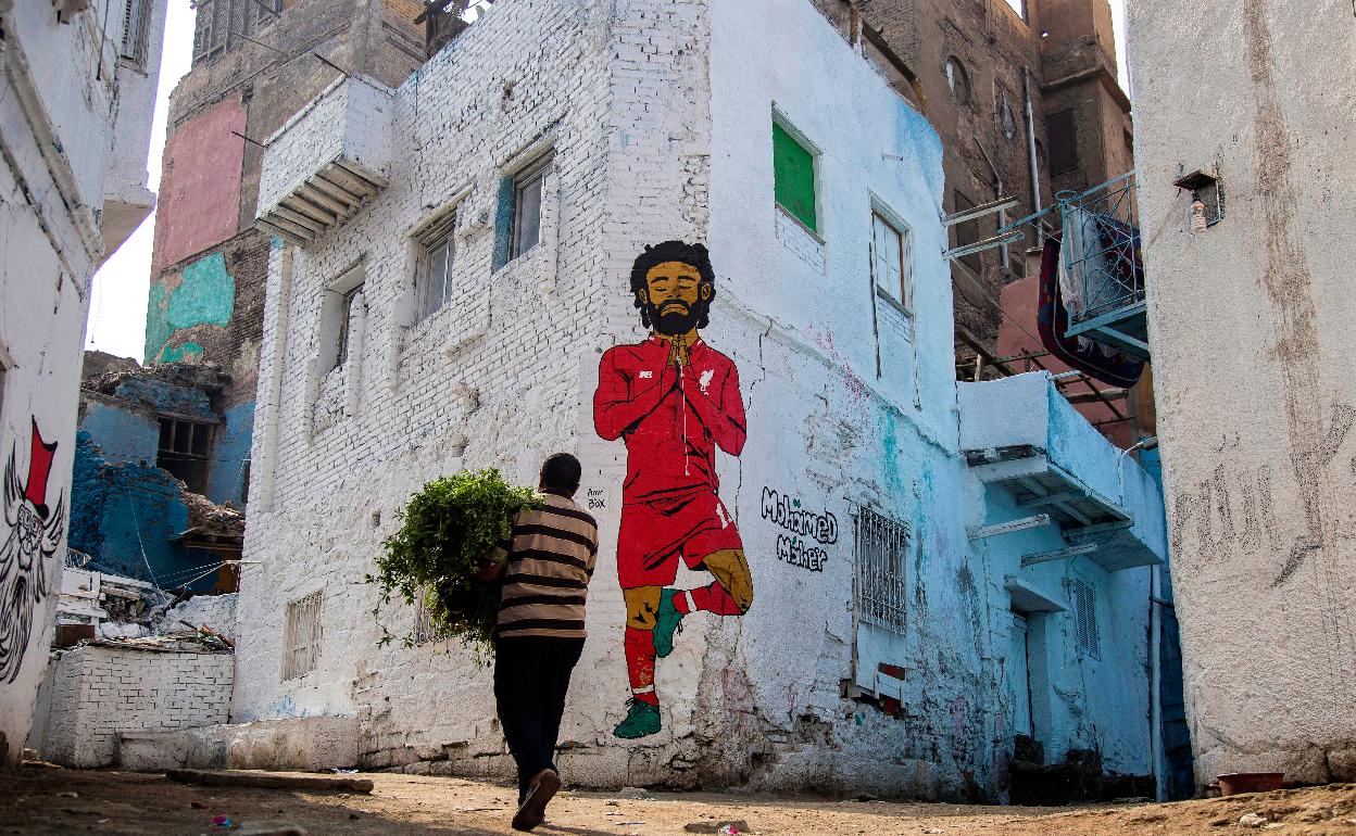 Un hombre camino delante de un mural del delantero egipcio Mohamed Salah en El Cairo