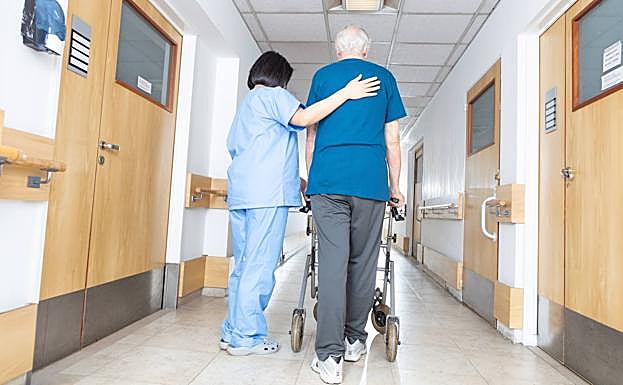 Un hombre mayor recibe la ayuda de una trabajadora en una residencia. 