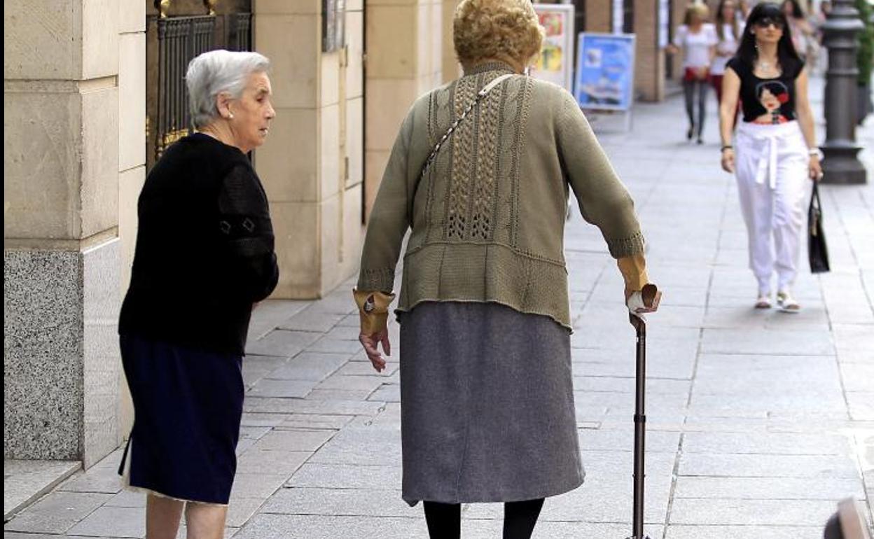 Dos personas mayores caminan por la calle. 