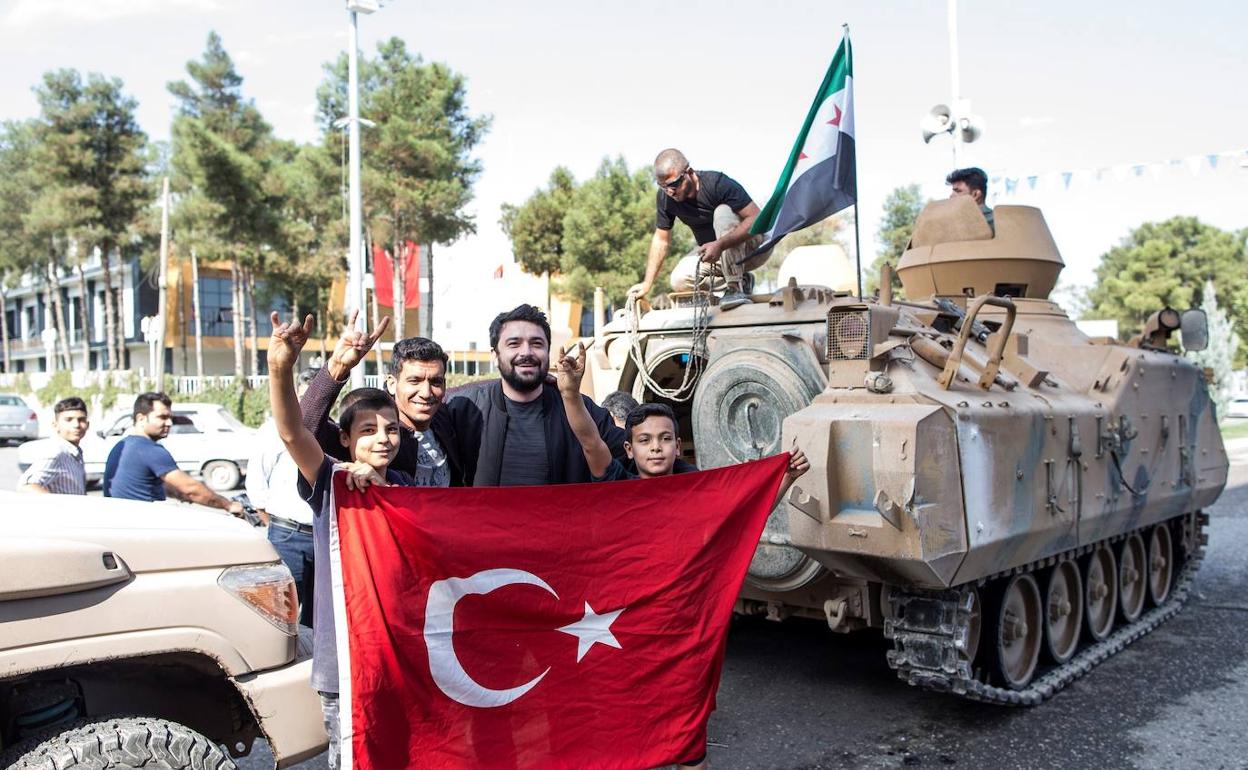 Civiles posando con una bandera turca junto a un carro de combate.