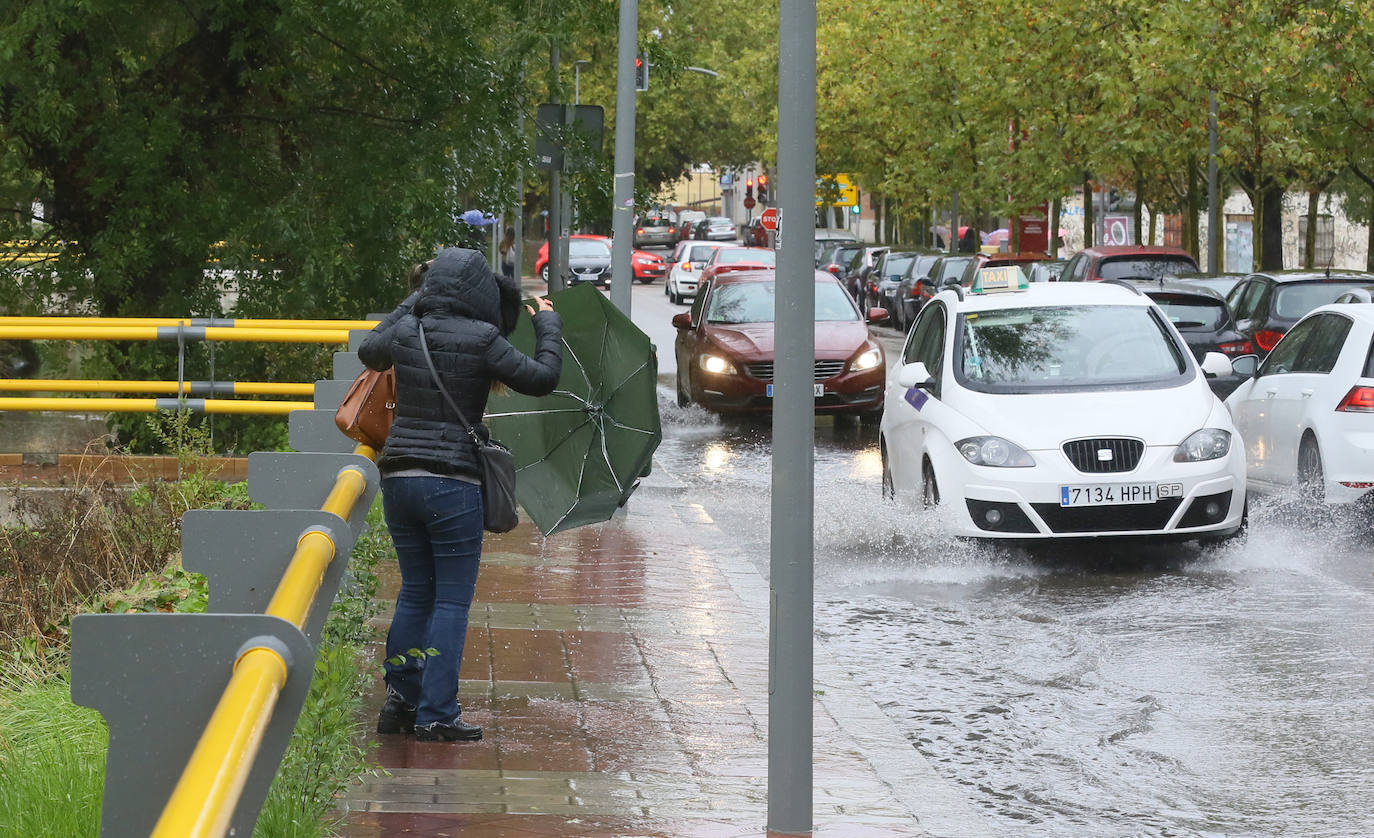 Dos viandantes se protegen de las salpicaduras de los coches en el paseo del Cauce. 
